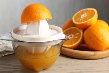 Meyve suyu. Meyve sıkacağı ve taze portakallar ahşap masada, yakın plan.