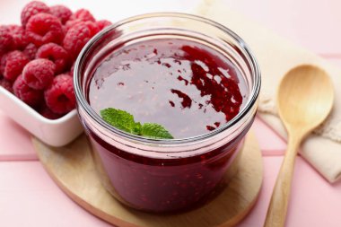 Cam kavanozda tatlı ahududu reçeli, pembe ahşap masada nane ve böğürtlen, yakın plan.