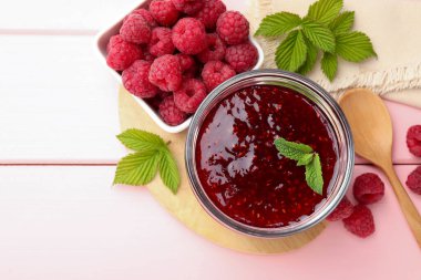 Tatlı ahududu reçeli cam kavanozda, böğürtlen ve nane şekeri pembe ahşap masada, düz yerde