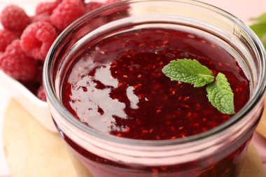 Cam kavanozda tatlı ahududu reçeli, masada çilek ve nane, yakın plan.