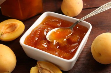 Lezzetli kayısı reçeli kaşık ve ahşap masada taze meyveler, yakın plan.