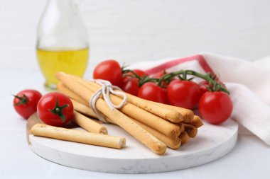 Lezzetli Grissini çubukları ve taze domatesler beyaz masada, yakın plan.