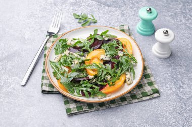 Lezzetli salata roka, mavi peynir ve sebzeler gri desenli masada.