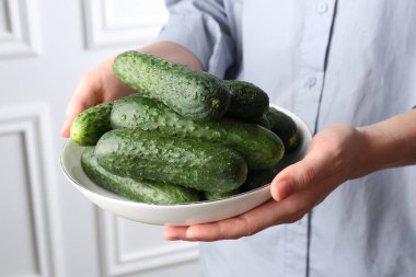 Beyaz duvarın yanında taze salatalıklı bir kadın, yakın plan.