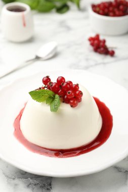 Kırmızı üzümlü lezzetli panna cotta, beyaz mermer masada sos ve nane, yakın plan.
