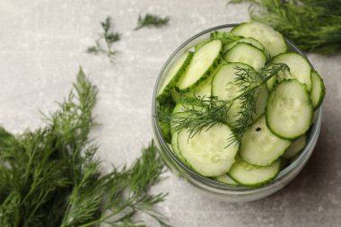 Turşu yapıyorum. Açık kavanozda taze salatalık dilimleri ve gri desenli masada dereotu.