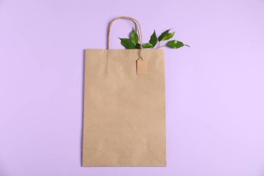 Çevre dostu ambalaj. Karton etiketli kağıt çanta ve menekşe arkaplanda yapraklar, üst görünüm