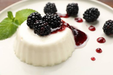 Lezzetli panna cotta böğürtlenli, nane ve sos masada, yakın plan.