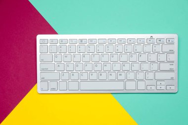 Renk arkaplanı üzerinde modern beyaz kablosuz klavye, üst görünüm