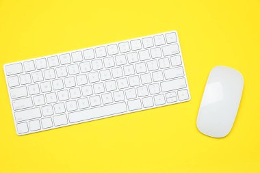 Sarı zemin üzerinde modern beyaz kablosuz klavye ve fare, üst görünüm