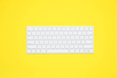 Sarı arkaplanda modern beyaz kablosuz klavye, üst görünüm