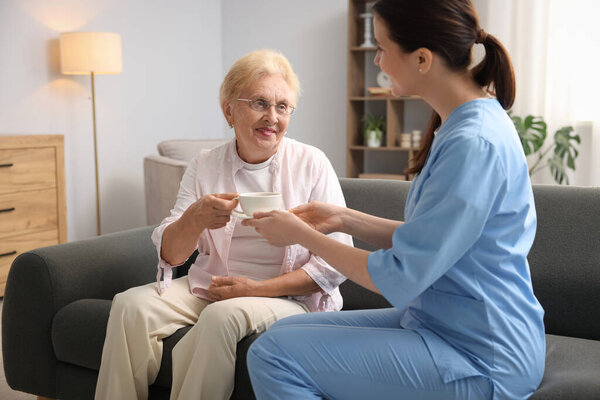 Nurse giving cup of drink to senior woman indoors. Home health care service