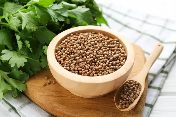 Kişniş tohumu ve taze kişniş beyaz ahşap masada, yakın plan.