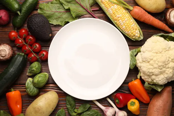 Sağlıklı vejetaryen yemekleri. Tahta masanın üzerinde farklı ürünlerle çevrili boş bir tabak.