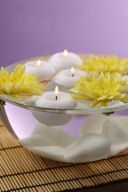 Mumları ve çiçekleri bir kase suyla yakmak bambu hasırında mor arka plana karşı, yakın plan