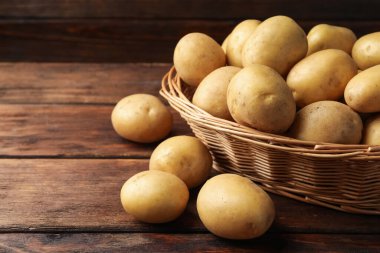 Tahta masada bir sürü çiğ patates ve hasır sepet, yakın plan.