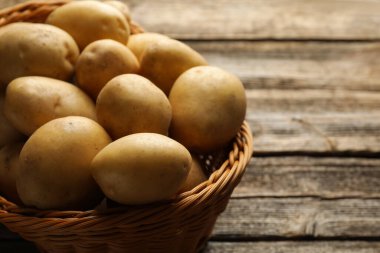 Tahta masada hasır sepetin içinde bir sürü çiğ patates, yakın plan.