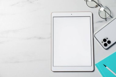 Tablet, akıllı telefon, gözlük ve kırtasiye malzemeleri beyaz mermer masa, düz yatak. Metin için boşluk