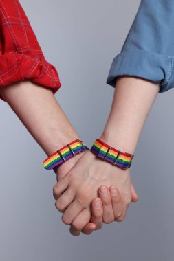 LGBT konsepti. Gökkuşağı bileklikli kadınlar açık gri arka planda el ele tutuşuyorlar, yakın plan.