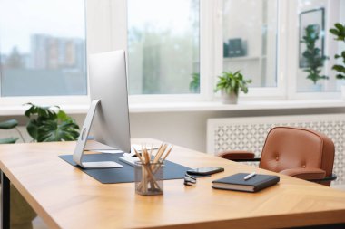 Modern bilgisayarı ve ahşap masa üzerindeki kırtasiyesi olan şık bir iş yeri.