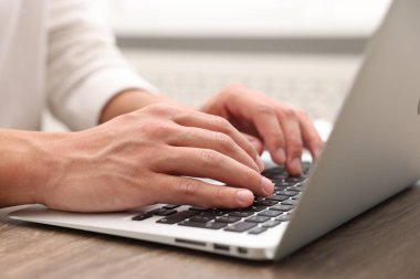 Kapalı alandaki ahşap masada dizüstü bilgisayar kullanan metin yazarı