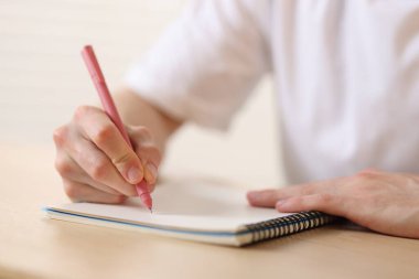Ahşap masadaki kalemle arka planı bulanıklaştıran, yakın plan, not defterine yazan adam