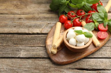 Lezzetli mozzarella peyniri topları, domatesler, fesleğen ve grissini ahşap masada. Metin için boşluk