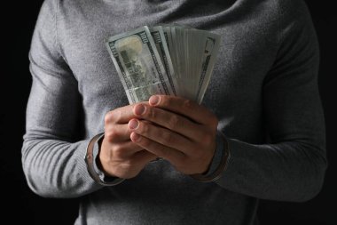 Yozlaşma. Elleri kelepçeli bir adam siyah arka planda dolarları tutuyor.