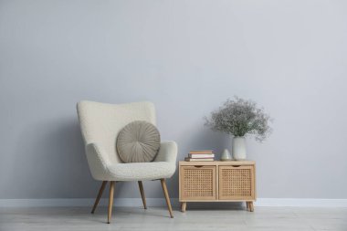 Açık gri duvarın yanında rahat bir koltuk ve dekor.