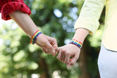 LGBT konsepti. Gökkuşağı bileklikli kadınlar dışarıda el ele tutuşuyorlar, yakın plan.