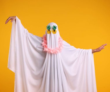 Komik hayalet. Güneş gözlüklü beyaz çarşaflı adam ve turuncu arka planda dans eden çiçek çelengi.