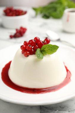 Kırmızı üzümlü lezzetli panna cotta, beyaz mermer masada sos ve nane, yakın plan.