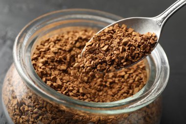 Koyu renkli masada kaşıktan kavanoza granüle kahve ekliyorum.