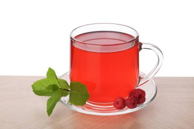 Aromatik ahududu çayı cam fincanda, böğürtlen ve yeşil yapraklar ahşap masada beyaz arka planda