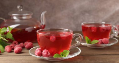 Cam bardaklarda ahududu çayı, çaydanlık, böğürtlen ve nane şekeri ahşap masada, yakın plan.