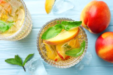 Şeftalili buzlu çay ve açık mavi ahşap masada nane.