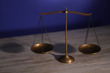 Ahşap masanın üzerindeki adalet terazileri karanlık arka planda.