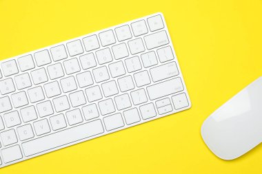 Sarı zemin üzerinde modern beyaz kablosuz klavye ve fare, üst görünüm