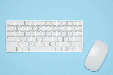 Açık mavi zemin üzerinde modern beyaz kablosuz klavye ve fare, üst görünüm
