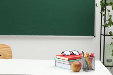 Farklı okul kırtasiyesi, bardaklar ve elmalar beyaz masada, kapalı alanda yazı için yer var.