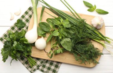 Farklı taze otlar, yeşil soğanlar ve sarımsak beyaz ahşap masa, düz uzanmış.