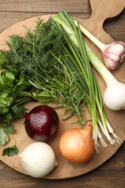 Farklı taze otlar, soğanlar ve sarımsak, ahşap masa, üst manzara.