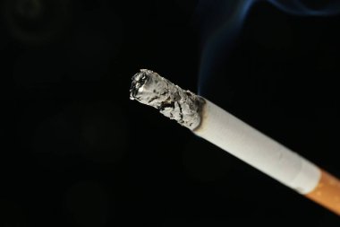 Siyah arka planda yanan bir sigara, yakın plan. Metin için boşluk