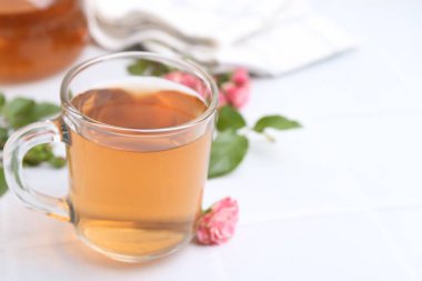 Cam bardakta romatik çay, güller ve yeşil yapraklar beyaz masada, yakın plan. Metin için boşluk