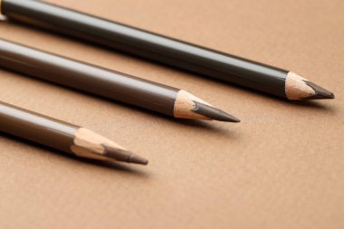 Kahverengi arka planda farklı kaş kalemleri, yakın plan.