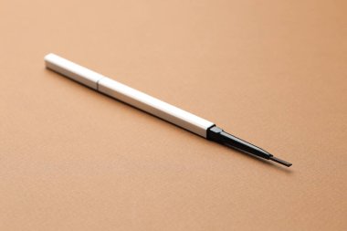 Kahverengi arka planda otomatik kaş kalemi, yakın plan.