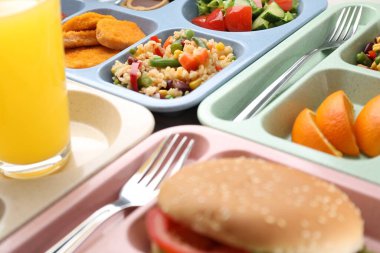 Lezzetli yiyecekler ve portakal suyu olan plastik tepsiler, yakın plan. Okul yemeği.