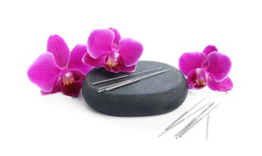 Akupunktur iğneleri, orkide çiçekleri ve beyaza izole edilmiş spa taşları.