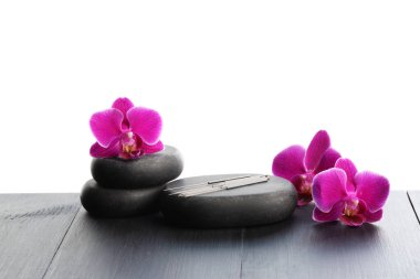 Akupunktur iğneleri, orkide çiçekleri ve beyaz arka plana karşı gri ahşap masa üzerindeki spa taşları