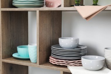 Beyaz duvarın yanında farklı bulaşık takımları olan raf ünitesi, kapalı.